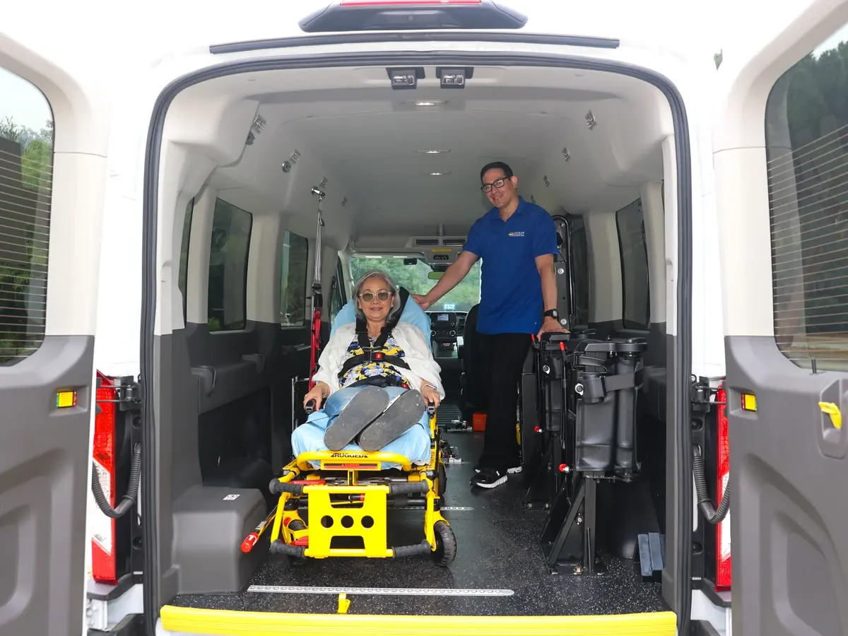 A rider reclined on a Stryker gurney inside a MoveMe Medical van with the driver at the rear doors