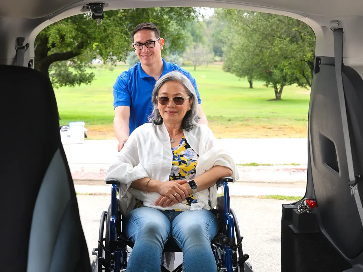 A smiling rider seated in her wheelchair inside a MoveMe Medical van with her driver behind her